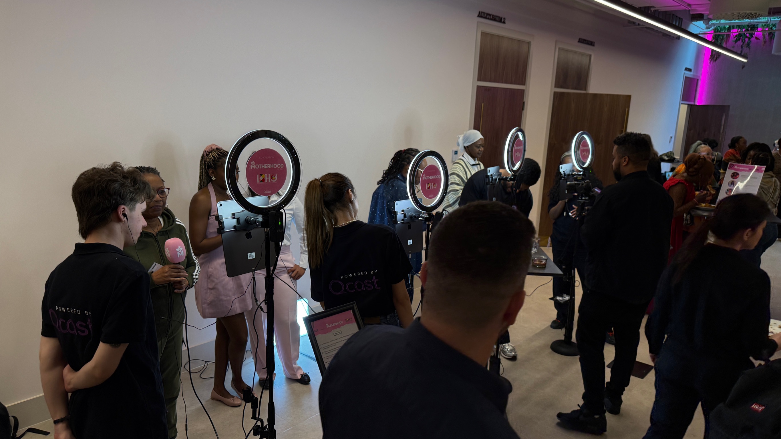 A group of people stand in front of ringlights at an event, holding microphones