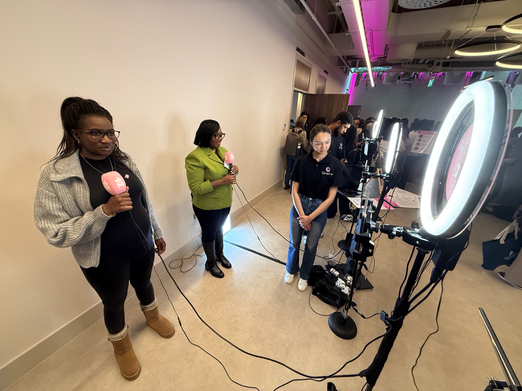 Tow Black women are holding pink microphones and speaking to iPads attached to ringlights