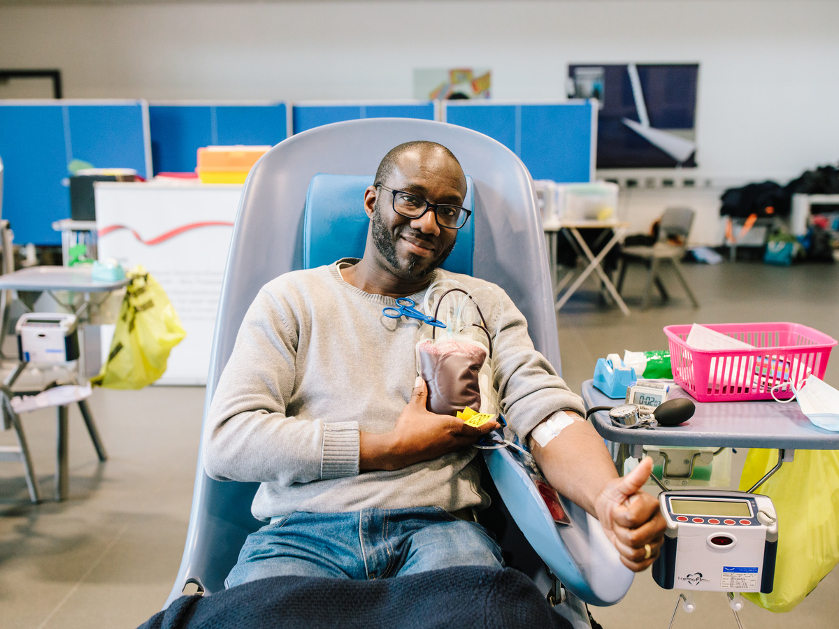 Volunteer laying on a bed smiling at the camera, with their thumb up giving a blood donation